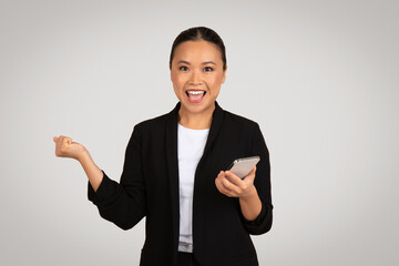 Exuberant Asian businesswoman in a blazer excitedly celebrating success with one hand raised