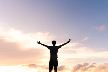 Fototapeta na wymiar Silhouette of a man with arms open against a beautiful sky, expressing gratitude for success and happiness