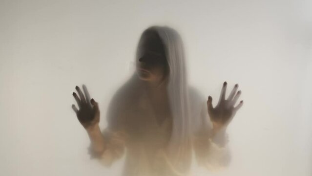 Silhouette of a woman behind a frosted glass or curtain in the fog. The ghostly woman touches the stele with her face and hands. HDR BT2020 HLG Material.