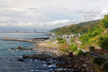 Fotobehang Scenery of a beautiful beach in Beiguan Tidal Park in Toucheng, Taiwan, with Taroko Express Train traveling on the railway, a coast highway along the rocky coastline & Yilan City on distant horizon © AaronPlayStation