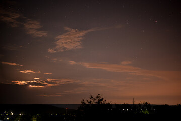 The moon rising through the clouds. Photographed with exposure time. Clouds in the dark. Forest silhouette at night