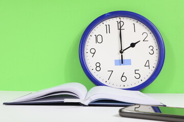 Wall clock with green background, open agenda, white sheet and cell phone.