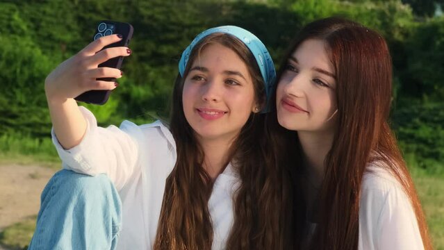 Happy sisters capture cherished moment with smartphone. Pleased young women create lasting memories during picnic in field