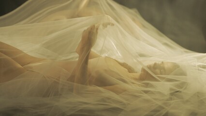 Side view of a young woman on a bed, under a transparent air cloth, close up. A woman illuminated...
