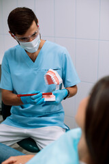 Male dentist shows dentures with a bracket in hands to the patient. False teeth in the hands