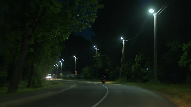 Traffic of motorcycles and minibus on night highway with rows of lanterns and trees