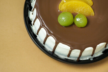Close up of a creamy butter cake topped with milk chocolate and decorated with two white grapes and...