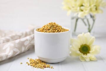 Fresh bee pollen granules and flower on white table