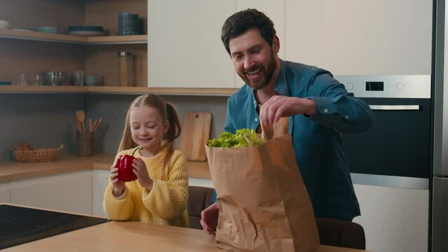 Happy family Caucasian father with kid girl unpacking shopping reusable eco bag little 10s child daughter help dad unpack red paprika yellow pepper bread tomato vegetables ordering goods food delivery