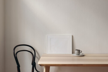 White landscape picture frame mockups on wooden table. Cup of coffee, vintage chair. White wall...