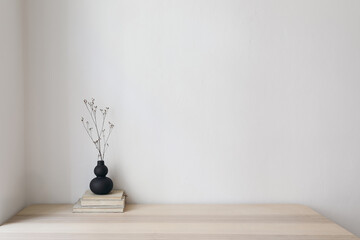 Elegant interior still life, minimal home design concept. Organic shaped black vase with dry grass on table, desk with old books. Working space, home office decor. Empty beige wall mockup. - obrazy, fototapety, plakaty
