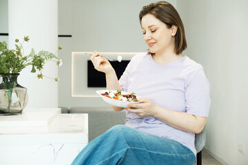 Charming plump female eating vegetable salad in modern kitchen