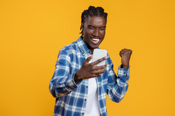 Cheerful excited young black man with smartphone celebrating success