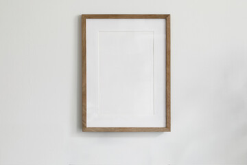 Single picture mockup poster hanging in the middle of white wall. Portrait large 50x70, 20x28, a3,a4. Empty wooden frame mockup. Clean, modern, minimal design. Indoor interior decor, show text, or