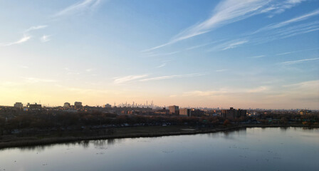 Fototapeta na wymiar nyc skyline view in the distance at sunset (aerial drone shot from corona flushing meadows park in queens) midtown manhattan skyscrapers silhouette at golden hour (meadow lake, water) far away