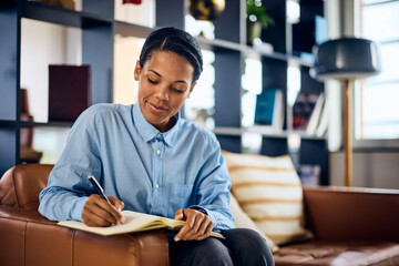 An African businesswoman taking some notes in her notebook, sitting on the sofa in her office.