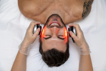 Dark-haired bearded man receiving phototherapy in a clinic