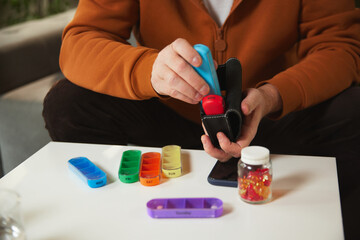 Person filling portable daily pill organizer from pill container, with other pill compartments. Concept of health and medical care, aging, medicine, treatment
