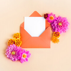 Orange envelope with clean white sheet for your text and flowers pink dahlias and marigolds on a beige background. Birthday greeting card, Valentine's Day, Mother's Day