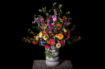 flower arrangement with colored silk flowers in vase. Black background. Studio photo.