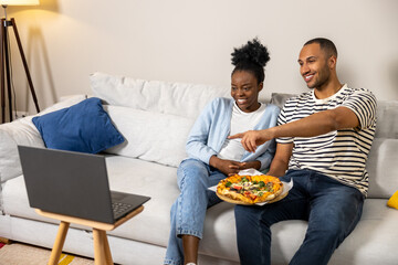 Man and woman using laptop for watching film while eating delicious pizza at home