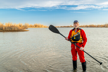 environmental portrait of a senior male paddler in a drysuit and life jacket holding stand up...