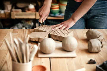 A potter makes marks on a piece of clay with a knife to soften it. Preparing for clay modeling in the workshop, close-up