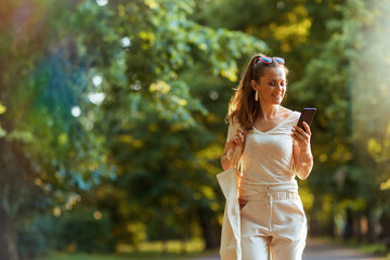 smiling trendy woman in shirt using phone and walking