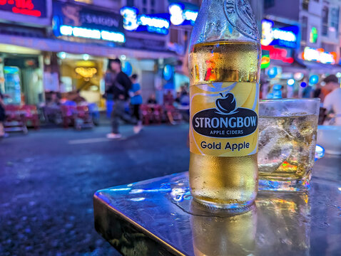 Ho Chi Minh City, Vietnam - Close-up of a cold bottle of Strongbow apple cider Gold Apple at a bustling outdoor pub in the heart of Bui Vien Street at night.