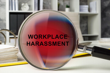 Office workspace and magnifying glass with words workplace harassment.