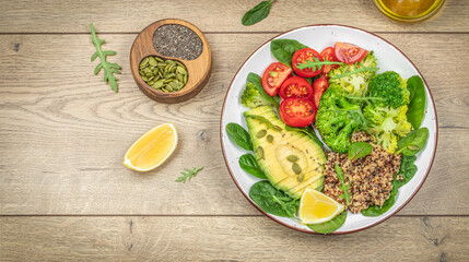 vegetable buddha bowl with quinoa, avocado, tomatoes, broccoli and spinach on wooden table, Clean eating dieting food concept, top view