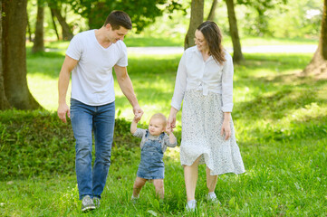 Fototapeta premium Happy family, dad, mom, child walk together in the park on a sunny summer day in nature, holding hands. Family vacation concept, first steps.