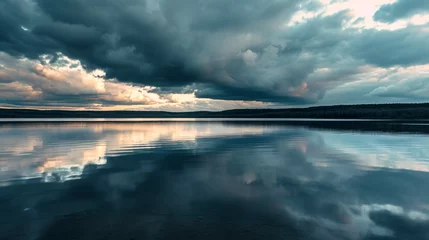  A calm lake reflecting the dramatic clouds of an approaching storm with darkening skies. © Leo