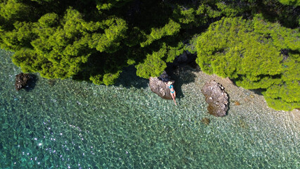 Aerial view of a girl on the rock in the sea. Vacation and adventure. Turquoise water. Top view from drone at ocean, azure watre and relax girl. Travel and relax image