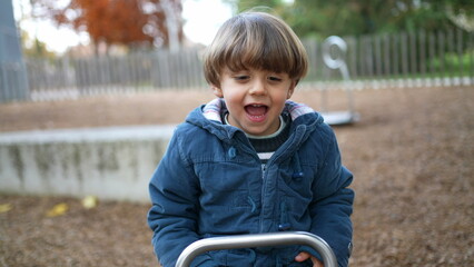 Joyful child plays at park on top of seesaw, Active 3 year old boy kid wearing blue jacket enjoys...