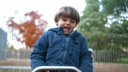 Joyful child plays at park on top of seesaw, Active 3 year old boy kid wearing blue jacket enjoys...