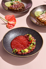 Elegant presentation of gourmet steak tartare with vibrant beetroot sauce in a black ceramic dish.