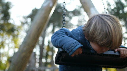 Playful Little Boy Twisting and turning while leaning on Park Swing during autumn fall park season. Carefree child engaged in play