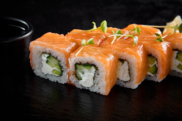 Philadelphia roll with salmon on a black slate, accompanied by soy sauce and wasabi