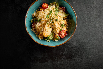 Top view of a quinoa salad with grilled chicken, cherry tomatoes, and mixed greens, served in a turquoise ceramic bowl