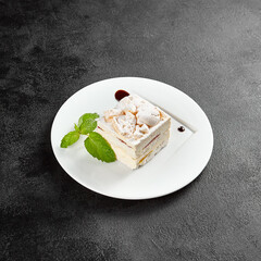 Delicate meringue cake with creamy cheese filling, garnished with a sprig of mint on a white plate