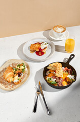 Gourmet breakfast spread with salmon croissant, skillet eggs, and pancakes with cappuccino and orange juice
