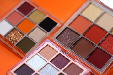 Colorful eyeshadow palettes and make up brush on orange background. Selective focus.