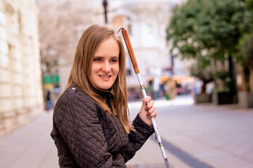 Close-up of a visually impaired woman holding a white cane and sitting on a bench in the city