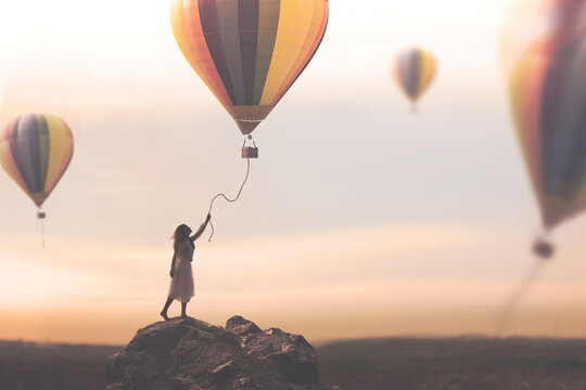 woman tries to catch the thread coming down from a hot air balloon that escapes free into the sky, concept of travel and adventure