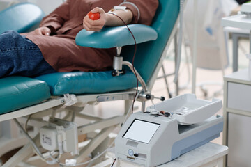 Unrecognizable hospital visitor donating blood into transparent bag placed on mixing machine