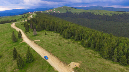 Aerial drone view of a car driving a mountainous high altitude road, along a spruce forest, on...