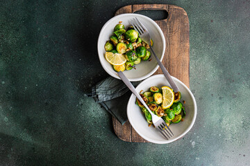 Top view of bowl of grilled Brussels sprouts seasoned with garlic and spices, garnished with a slice of lemon, served on a wooden board with a fork