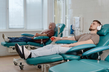 Caucasian man and muslim woman relaxing side by side in clinic during blood donation