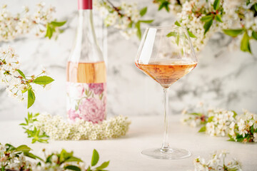 Rose wine glass against white wall with spring cherry flowers. Refreshing alcoholic summer drink or nature concept.